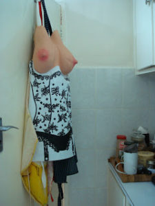 A joke cook's apron hangs from a peg. It has too large pink nippled rubber breasts protruding from the top.